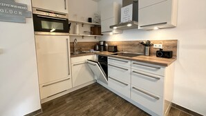 A modern kitchen with white cabinetry, a built-in oven, and a dishwasher. - Moin and welcome to Apartment Küstenglück! (Dangast)
