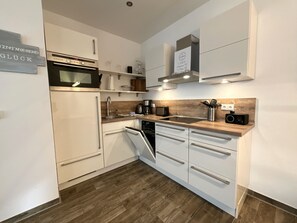 A modern kitchen with white cabinetry, a built-in oven, and a dishwasher. - Moin and welcome to Apartment Küstenglück! (Dangast)