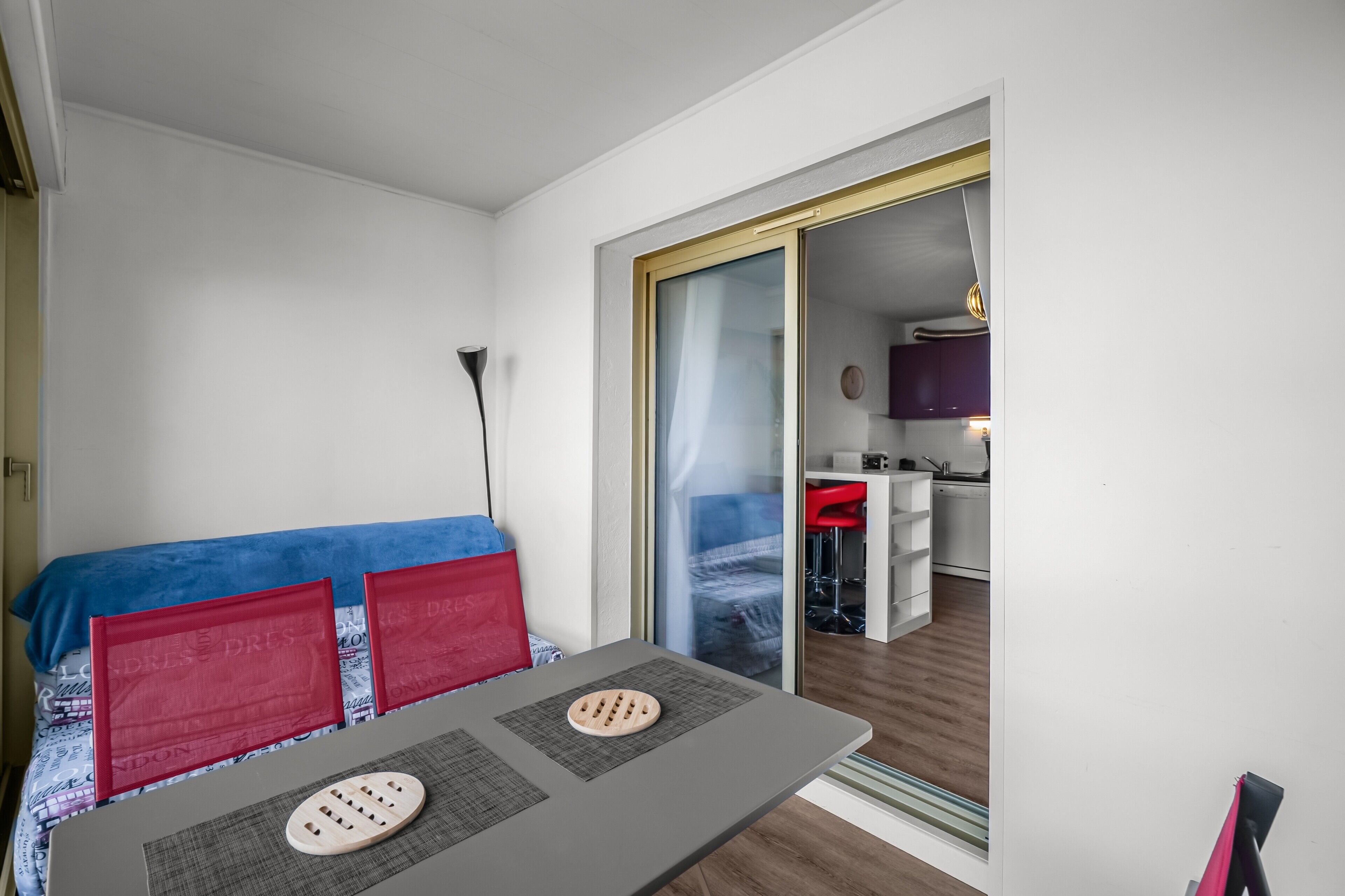 A compact room with a bed, a small table, and a sliding door leading to a kitchen area.