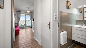 Habitación de hotel con piso de madera, puerta blanca y baño con lavamanos blanco, con vista al exterior.
