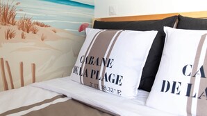 Ein Bett mit weißer Bettwäsche und zwei Kissen mit Aufschrift, ein Gemälde mit Strandmotiv und ein hölzernes Kopfteil.