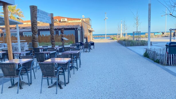 Ein Restaurant mit Terrassensitzgelegenheiten, einer Schautafel und Blick aufs Meer.