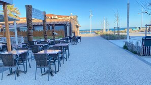 Restaurante com mesas ao ar livre, uma placa e vista para o mar.