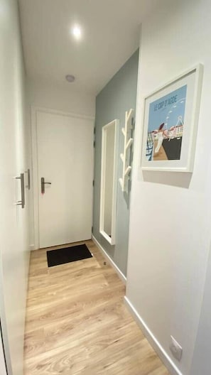A hallway with a wooden floor, a white door, and a framed picture on the wall. - Petit Bijou in the heart of Agde's port center (Agde)