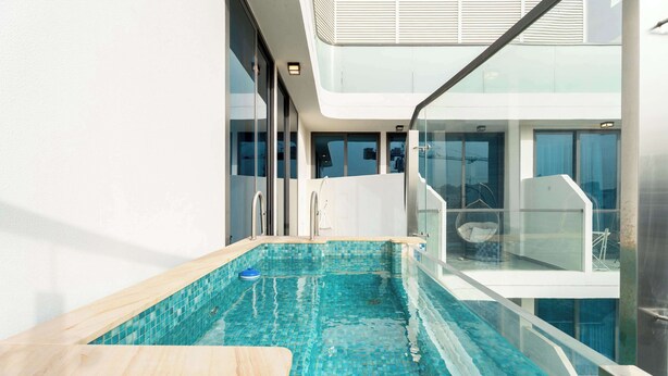 Ein moderner, überdachter Schwimmbereich mit klaren blauen Fliesen, einer Holzterrasse und einem Glasgeländer.