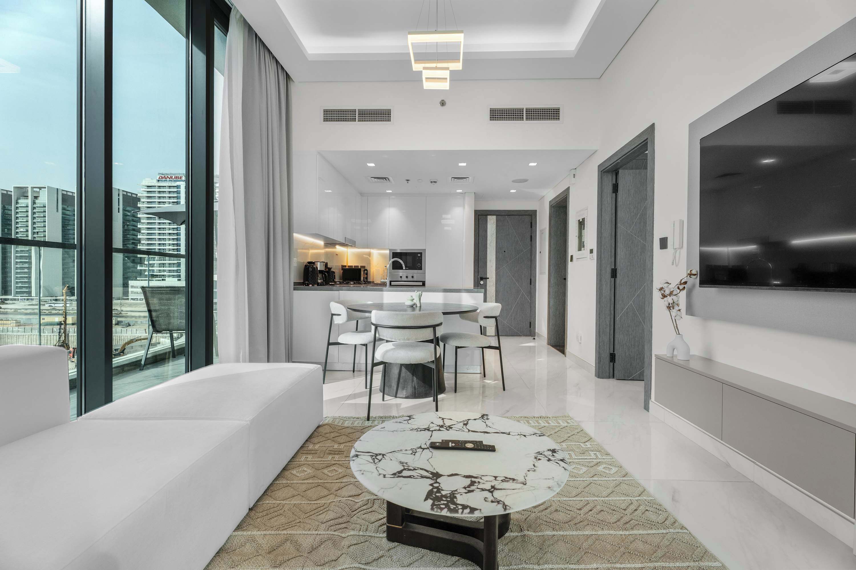 A modern living room with a large window, a dining area, and a kitchen.