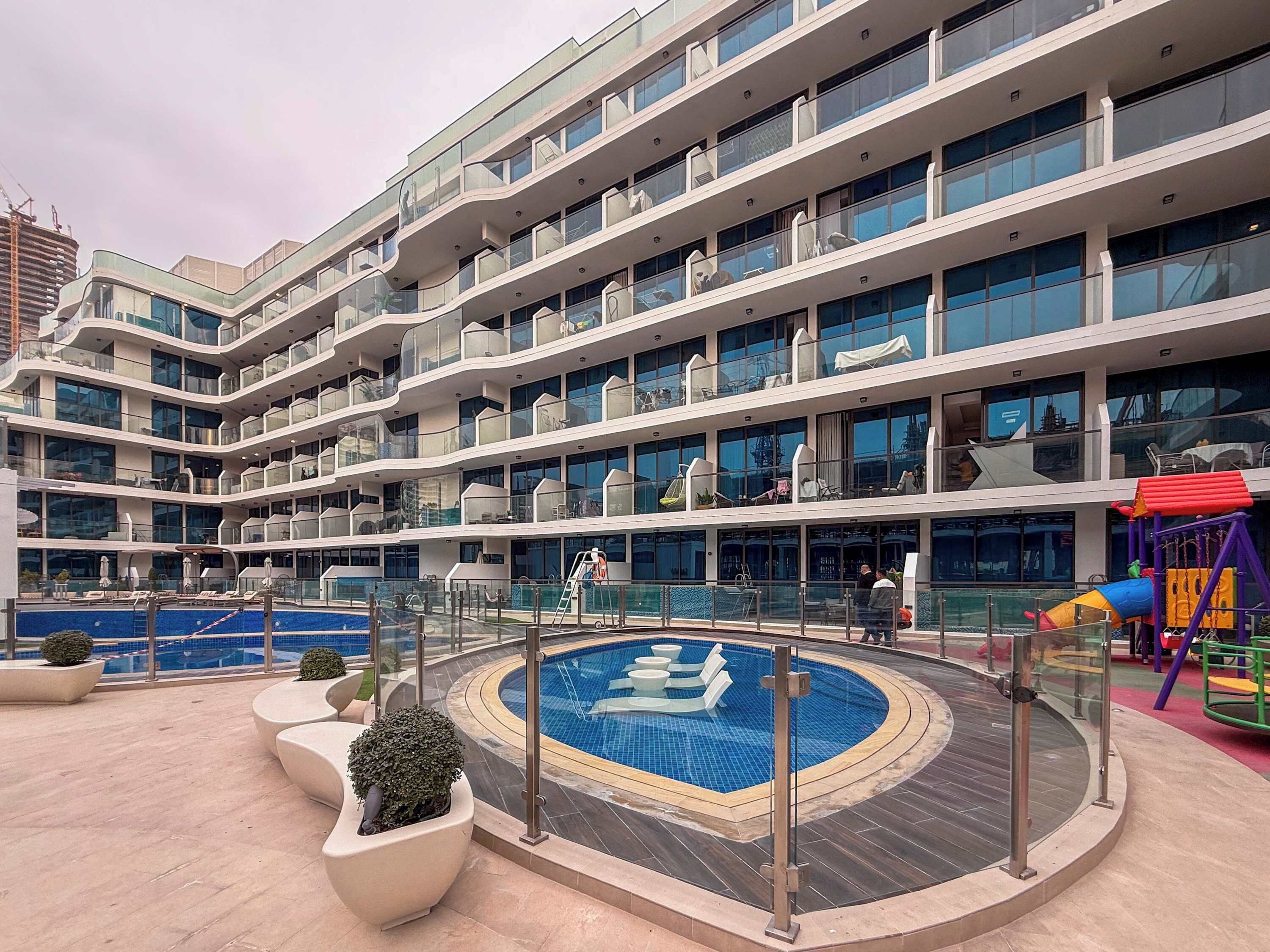 Un hôtel à plusieurs étages doté d’une piscine, d’un espace extérieur aménagé avec des sièges et d’un terrain de jeux.