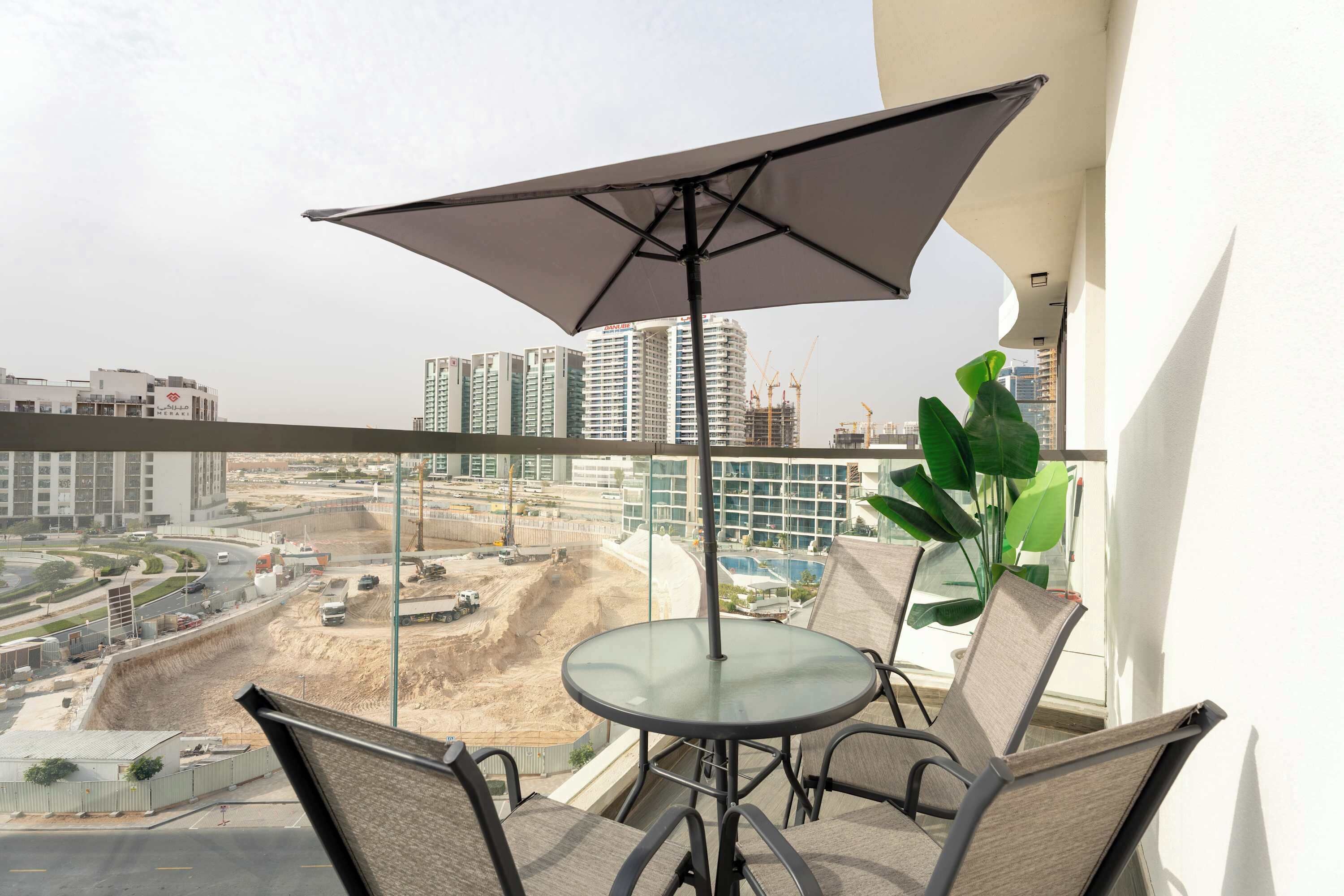 Ein Balkon mit Tisch und Stühlen, einem Sonnenschirm und Blick auf eine Stadt mit Gebäuden und Bauarbeiten.