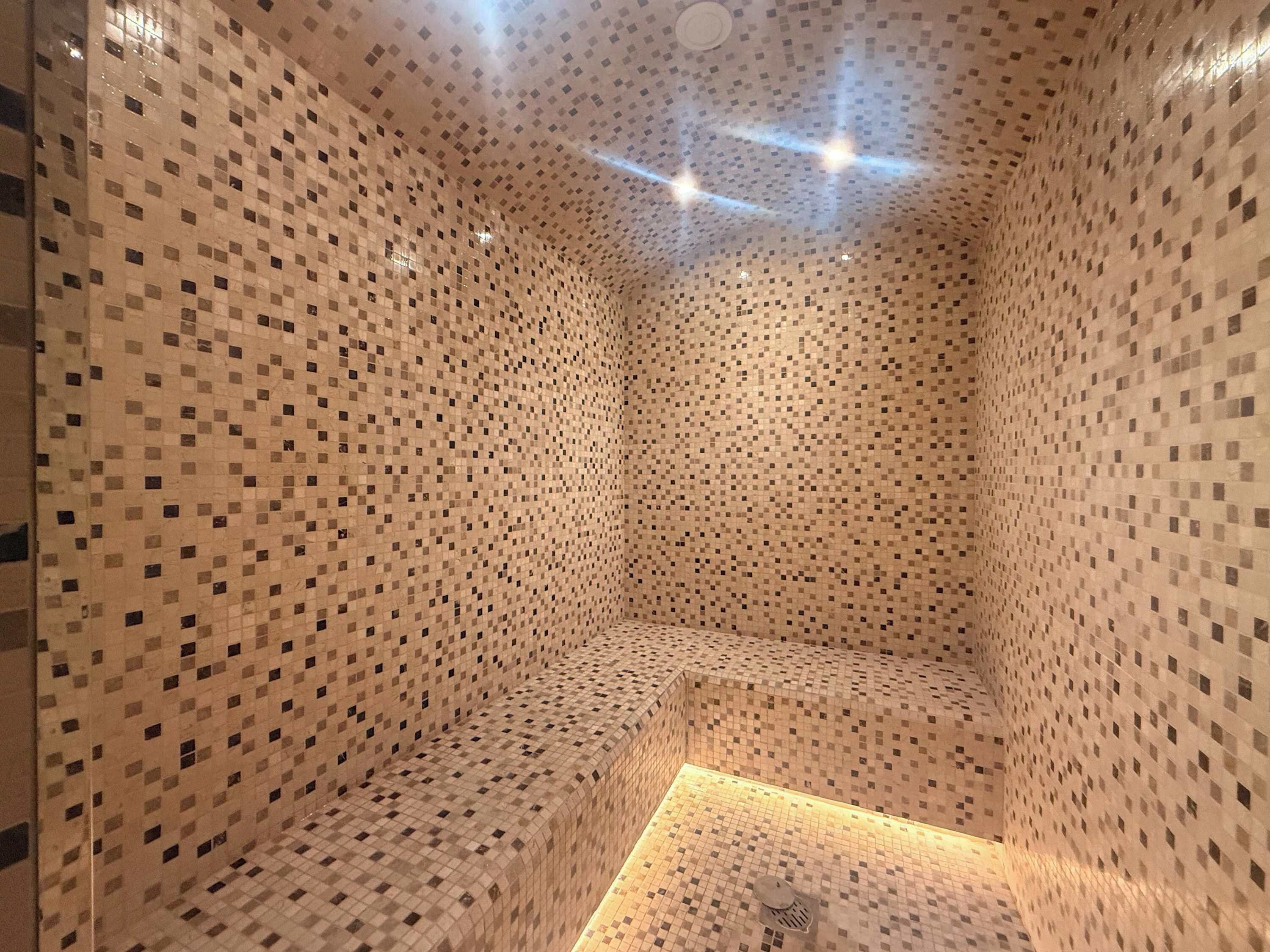 Een kamer met een betegelde mozaïekwand, een ingebouwde zithoek en een klein verlicht gedeelte op de vloer.