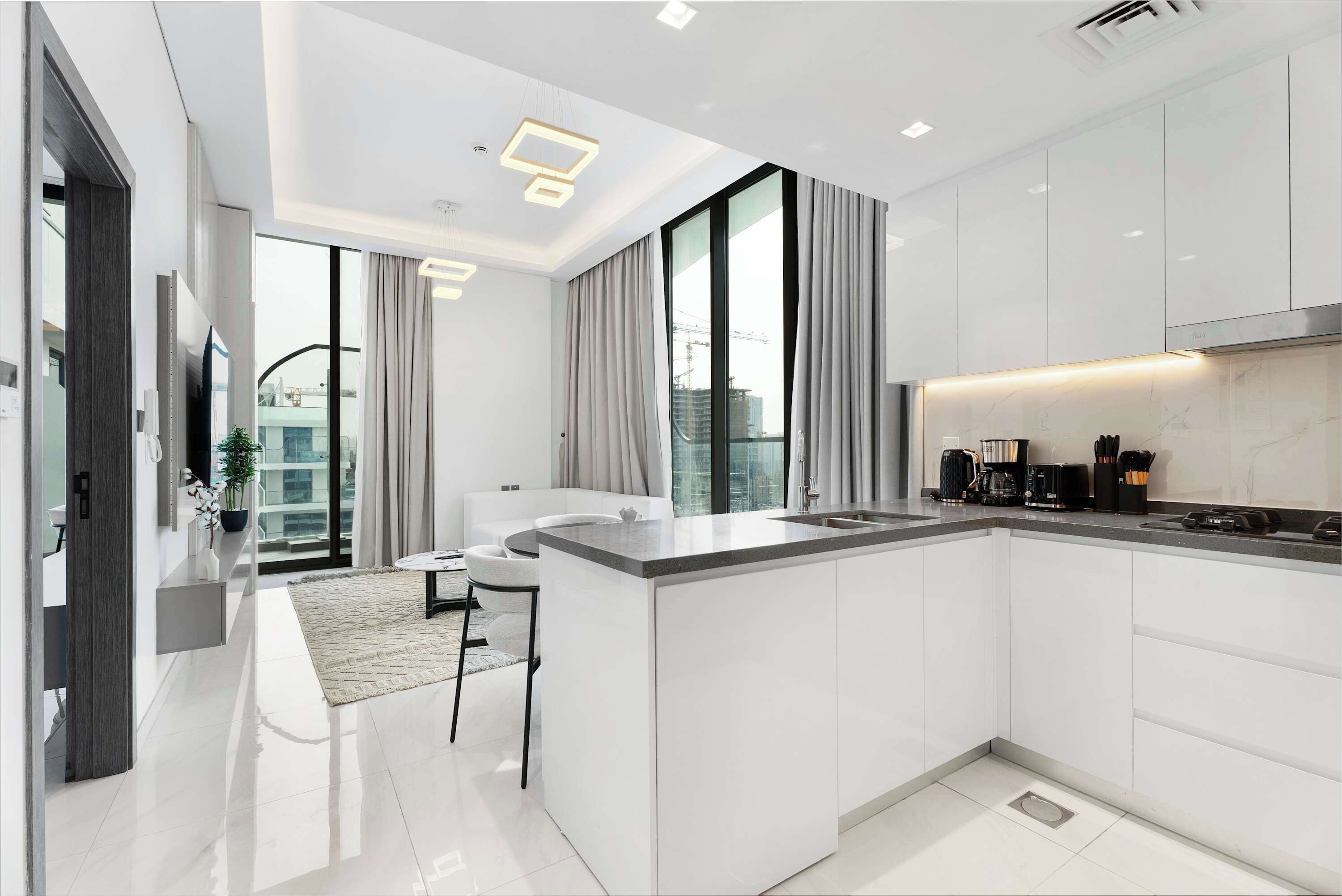 A modern kitchen with white cabinetry, a central island, and a dining area with a white table and chairs.