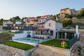 A modern house with a swimming pool, a patio with lounge chairs, and a view of a historic building in the background. - Villa Aurana Zadarvillas (Pakostane)