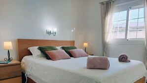 Cama bem arrumada com travesseiros, abajur e toalha enrolada sobre a cama.