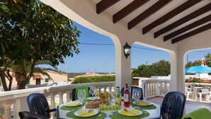 Uma sala de jantar com uma mesa posta para quatro, cadeiras de exterior e vista para a paisagem circundante.