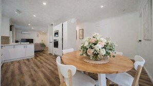 A dining area with a round wooden table, white chairs, and a floral centerpiece. - Serene Townsville Retreat with Pool & Alfresco, Sleeps 7 (Kirwan)