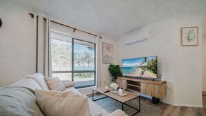 A modern living room with a large window, a flat-screen TV, a sofa, and a coffee table. - Serene Townsville Retreat with Pool & Alfresco, Sleeps 7 (Kirwan)