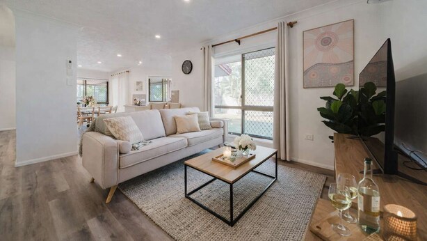 A modern living room with a sofa, coffee table, TV, and a dining area in the background. - Serene Townsville Retreat with Pool & Alfresco, Sleeps 7 (Kirwan)