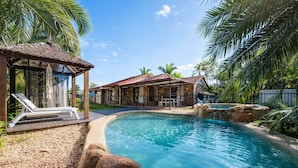 A swimming pool with lounge chairs, a gazebo, and a stone building with a tiled roof. - Serene Townsville Retreat with Pool & Alfresco, Sleeps 7 (Kirwan)
