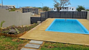 Ein rechteckiger Swimmingpool mit blauer Umrandung, umgeben von einer Betonplattform und einem Holenzaun.
