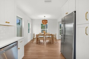 A modern kitchen with white cabinetry, a stainless steel refrigerator, and a dining area with a wooden table and chairs. - Beachside on B  - Updated cottage just steps to beach (St. Augustine Beach)