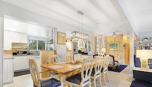 Eine moderne Küche mit weißen Schränken, ein Essbereich mit Holztischen und -stühlen sowie ein Wohnzimmer mit blauem Sofa und Dekoration.