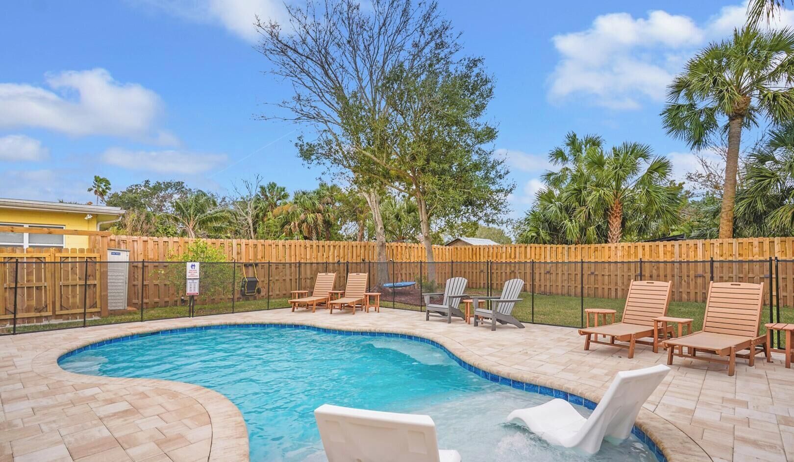A swimming pool with lounge chairs and a wooden fence.