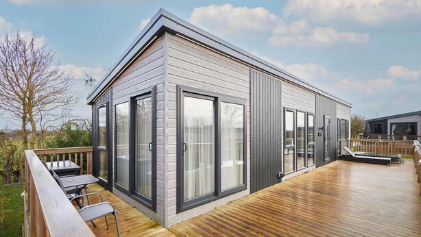 Een modern huis met grote schuifdeuren, een houten terras en een klein zitgedeelte buiten.