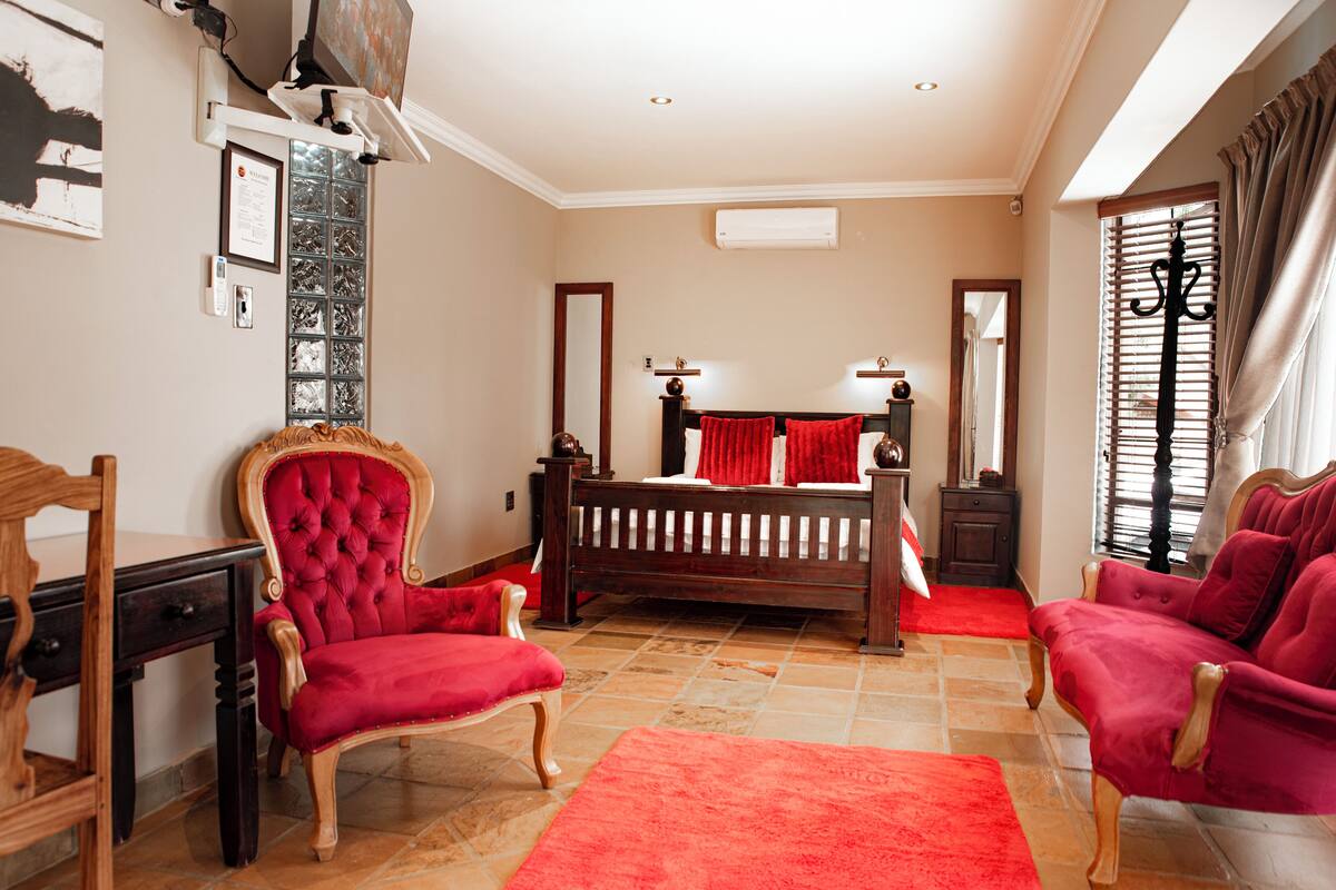 Une chambre à coucher avec un lit, deux fauteuils rouges, un bureau en bois et un tapis rouge.