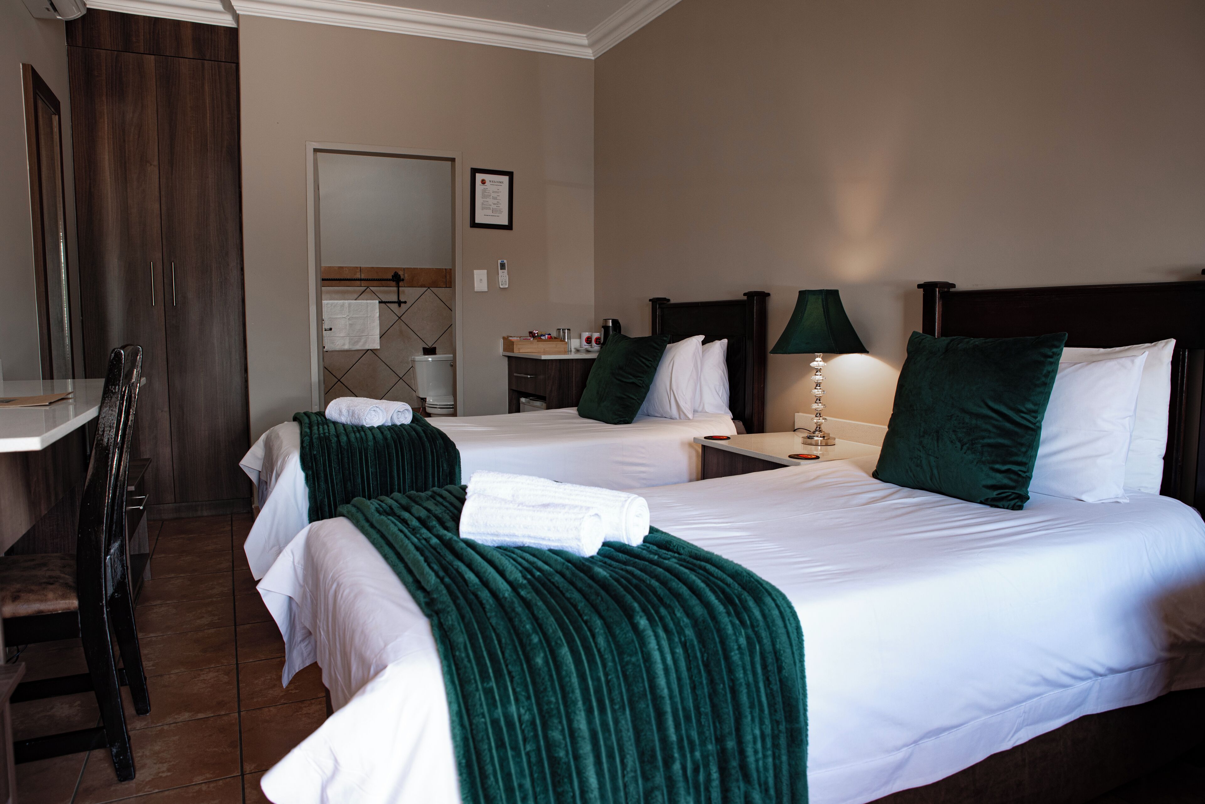 Een hotelkamer met twee bedden, een bureau, een stoel en een nachtkastje met een lamp.