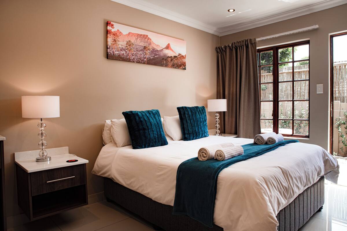 Une chambre d’hôtel avec un grand lit, deux tables de chevet avec des lampes, un tableau au mur et une vue par la fenêtre.