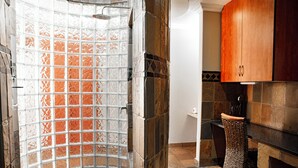 A bathroom with a glass shower enclosure, a wicker chair, and a wooden cabinet. - The Orion Guest House (Middelburg)