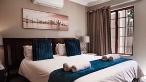 A neatly made bed with a cityscape painting above it, a window with curtains, and a bedside lamp. - The Orion Guest House (Middelburg)