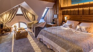 Een gezellige slaapkamer met een schuine kap, een groot bed, een zithoek met een fauteuil en een kleine tafel.