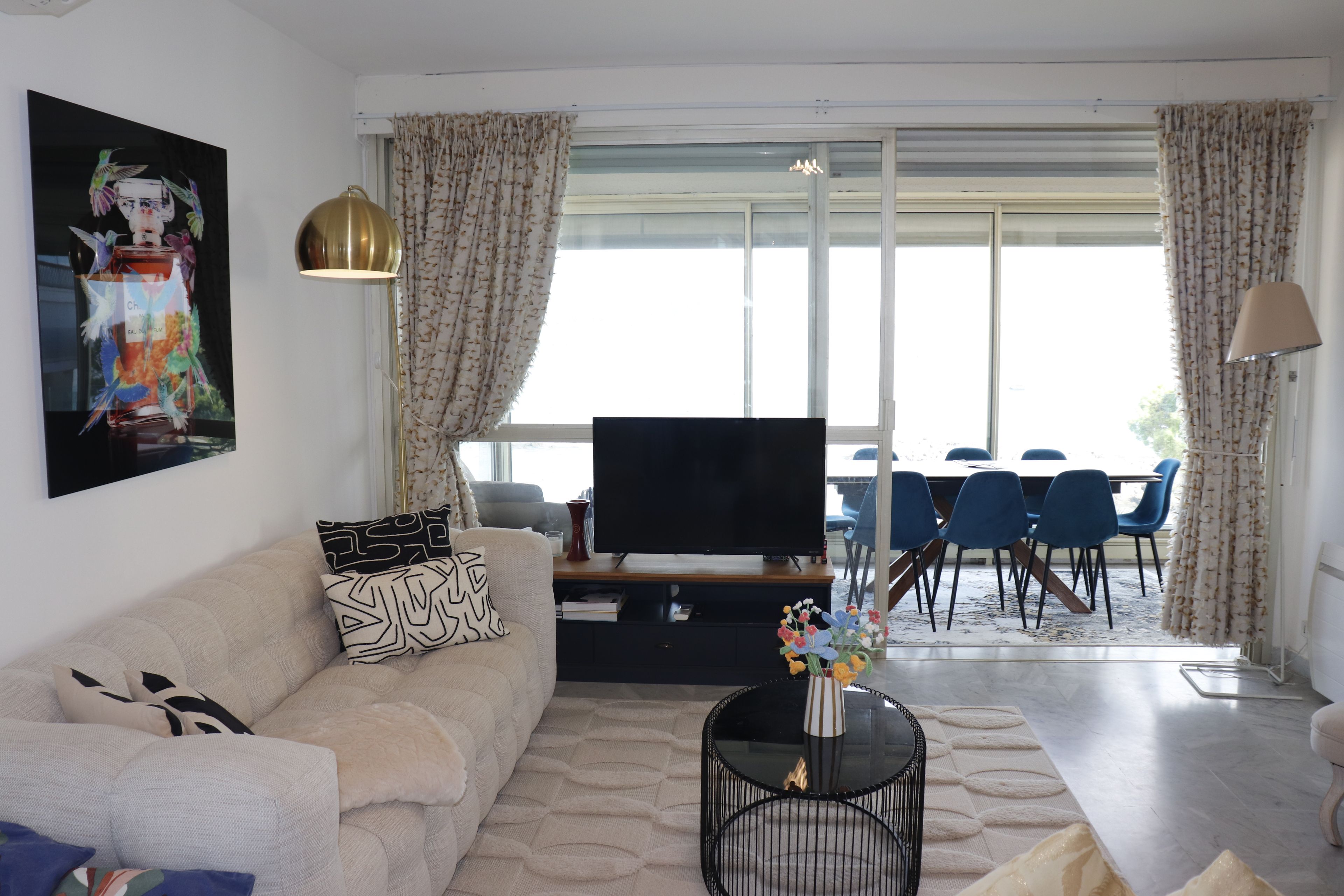 A modern living room with a sofa, a flat-screen TV, a coffee table, and a dining area with chairs and a table.