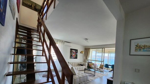 Un espacio habitable amplio con una escalera moderna, un conjunto de sofás y vista al mar.