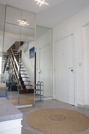 Una habitación con un espejo grande que refleja una escalera, una puerta y una alfombra pequeña.