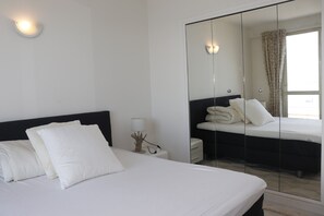 Ein Hotelzimmer mit Bett, Nachttisch, Lampe und einem großen Spiegel, der das Zimmer reflektiert.