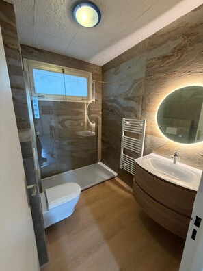 Ein Badezimmer mit Dusche, Toilette und Waschtisch mit Spiegel.