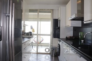 Una cocina moderna con electrodomésticos de acero inoxidable, un ventanal y una puerta que da a un balcón.