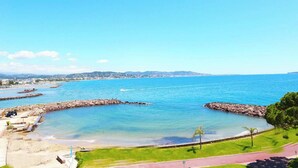 Vista costera con aguas azules cristalinas, un rompeolas rocoso y un horizonte urbano distante.