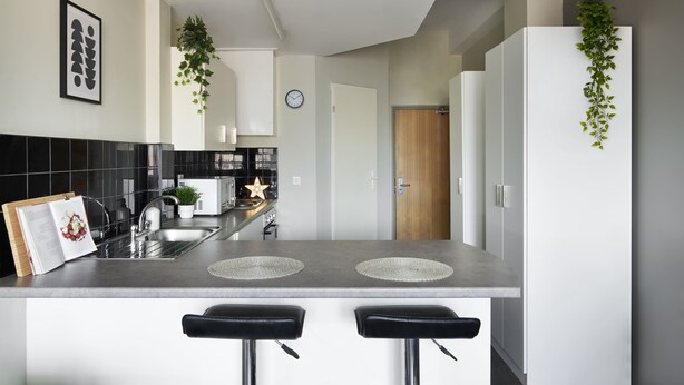 A modern kitchen with a central island, black bar stools, a microwave, and a clock on the wall. - For Students Only Rooms in Plymouth (Plymouth)