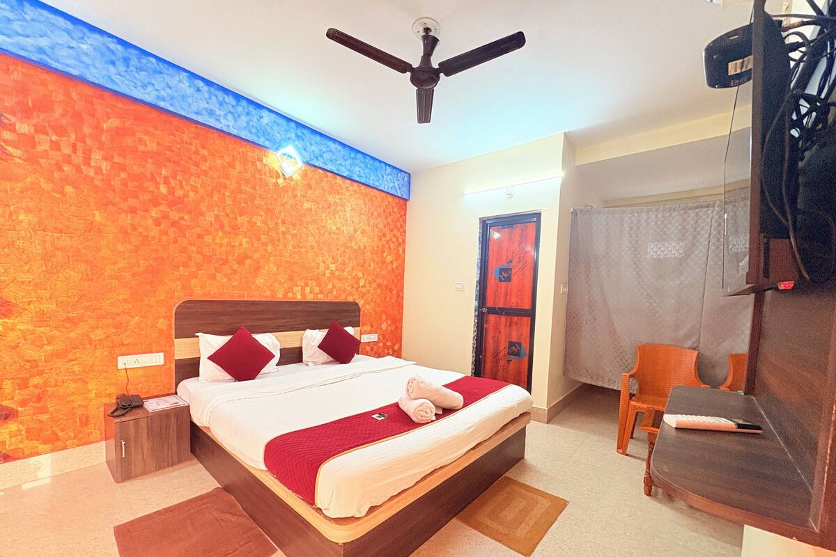 A hotel room with a large bed, a ceiling fan, a desk with a chair, and a door with a curtain.