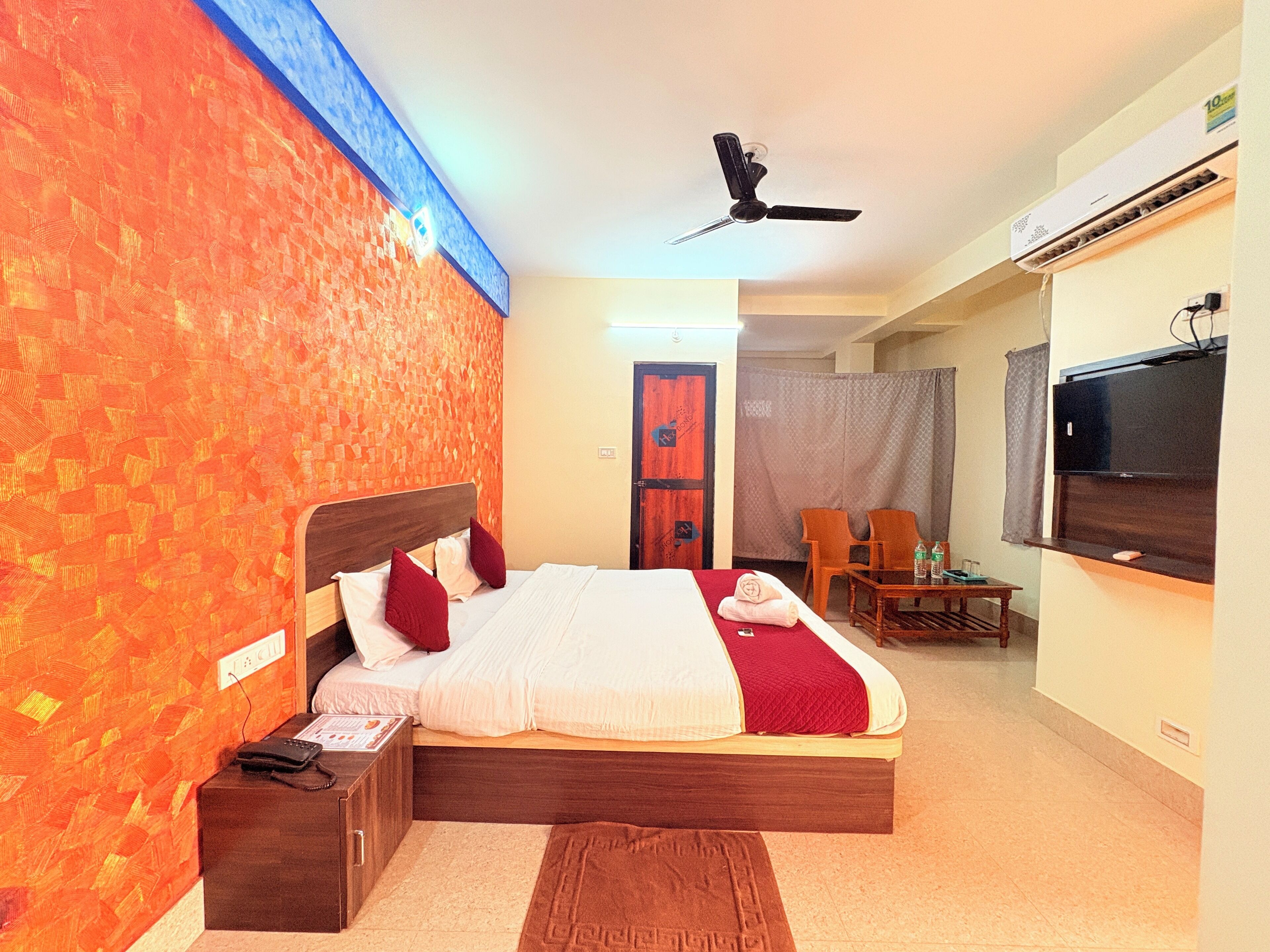 A hotel room with a bed, a desk, a chair, a TV, and an air conditioning unit.