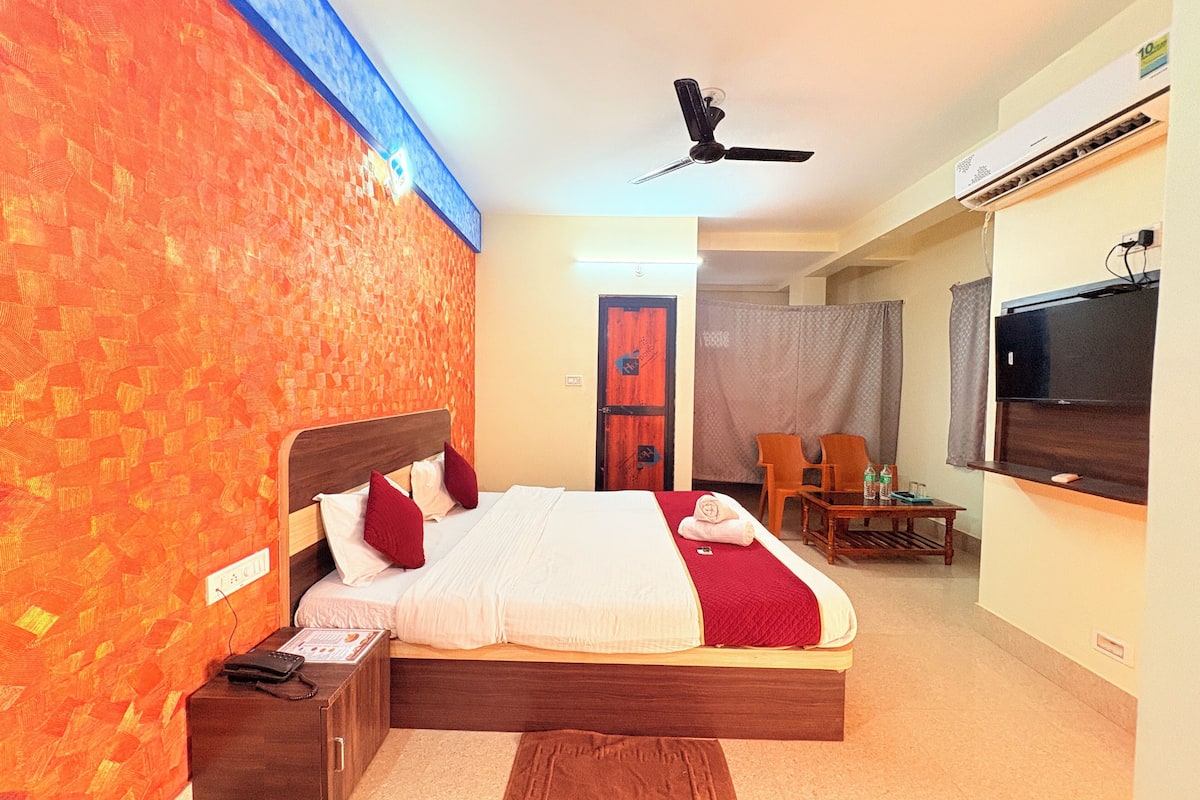 A hotel room with a bed, a desk, a chair, a TV, and an air conditioning unit.
