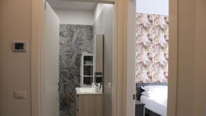 A narrow hallway leading to a bathroom with a marble backsplash and a small vanity with a mirror.