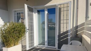 A patio with a white table and chairs, a potted plant, and a sliding glass door leading to a covered area.