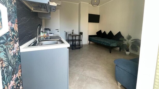 A compact living space with a kitchenette, a dining area, and a seating area with a sofa and a TV mounted on the wall.