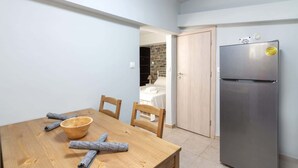 A compact kitchen with a modern stainless steel refrigerator, a wooden dining table with chairs, and a stone wall in the background. - Cozy Corner in Petralona (Athina)