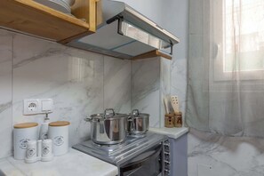 Une cuisine équipée d’une cuisinière, de casseroles et d’une hotte aspirante. On y trouve des bocaux étiquetés « Café Sweet Home » et « Sucre Sweet Home ».