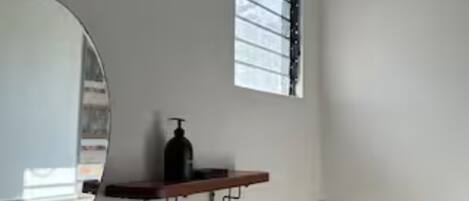 A bathroom with a toilet, a mirror, a window, and a shelf with toiletries.