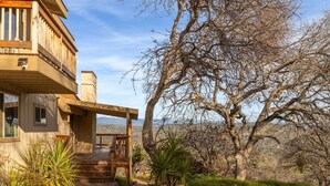 A two-story wooden house with a balcony, a stone fireplace, and a view of the surrounding landscape.